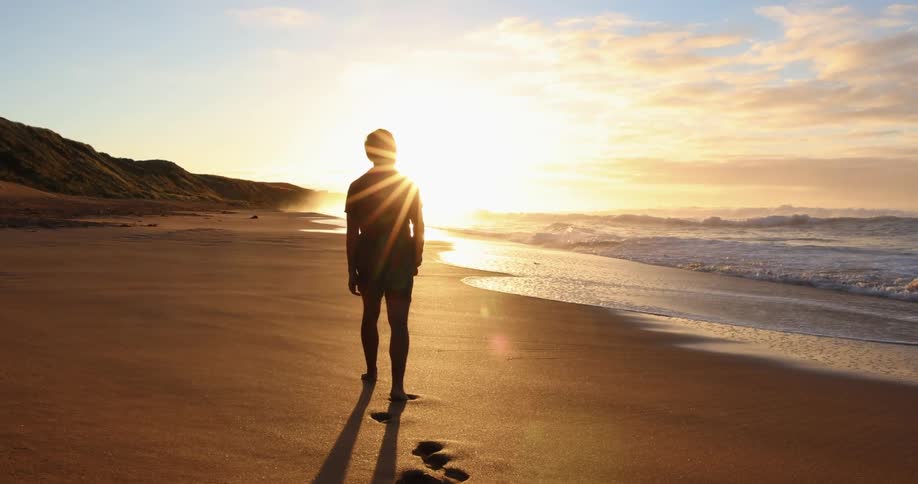 Man leaves footprints on beach as he walks toward sun on horizon