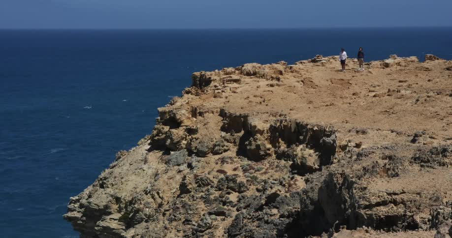 Two people standing on a cliff on the shore