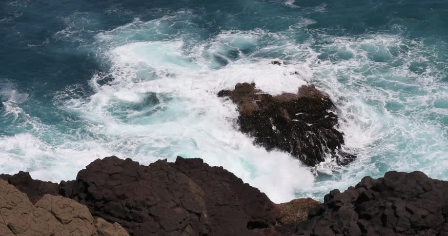 Waves crash against the large rocks on the coast
