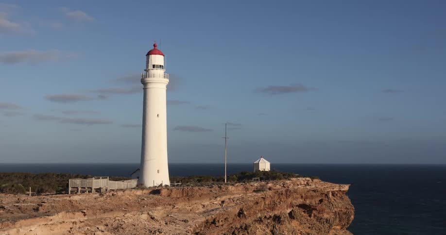 Tall narrow lighthouse stands on promontory as blue ocean stretches to horizon