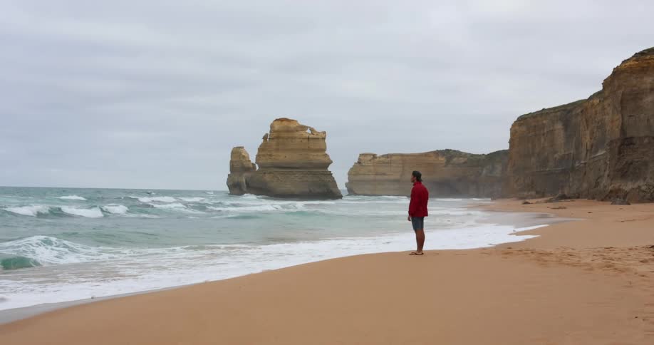 A man stands at the edge of the beach and watches waves move onto the shore