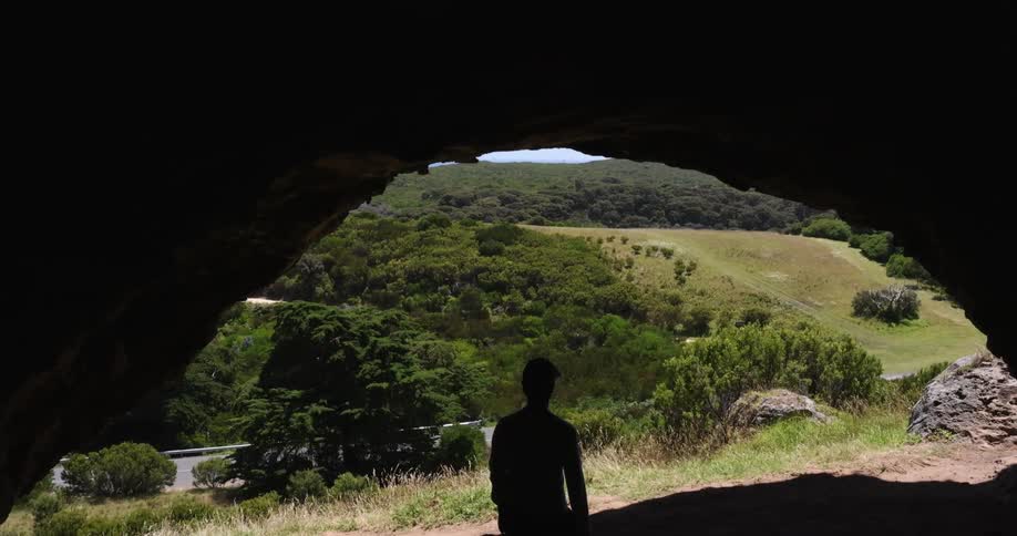A man staring out of a cave at some hills