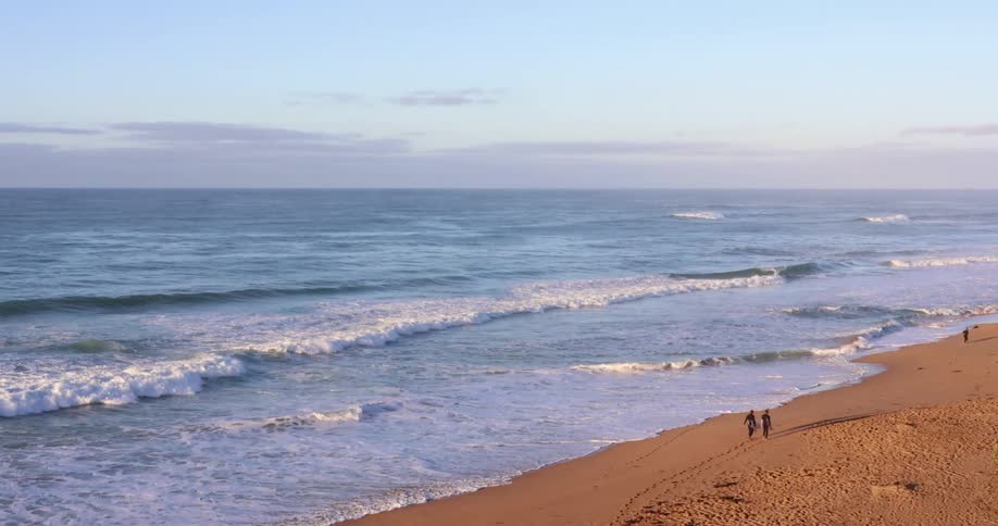 People walking on a beach with sand and waves with the ocean sky and clouds in the background