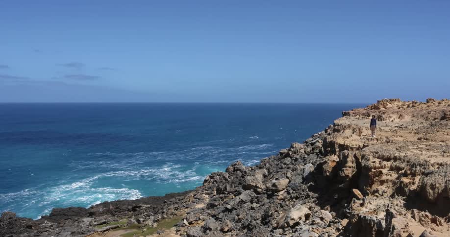 Person stands on promontory near blue ocean