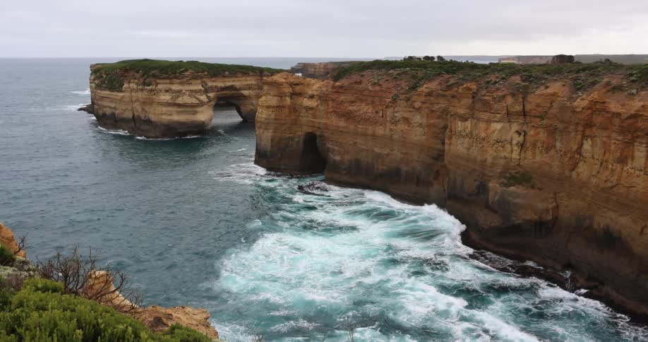 Ocean waves splash and break against the sheer cliffs and rock formations