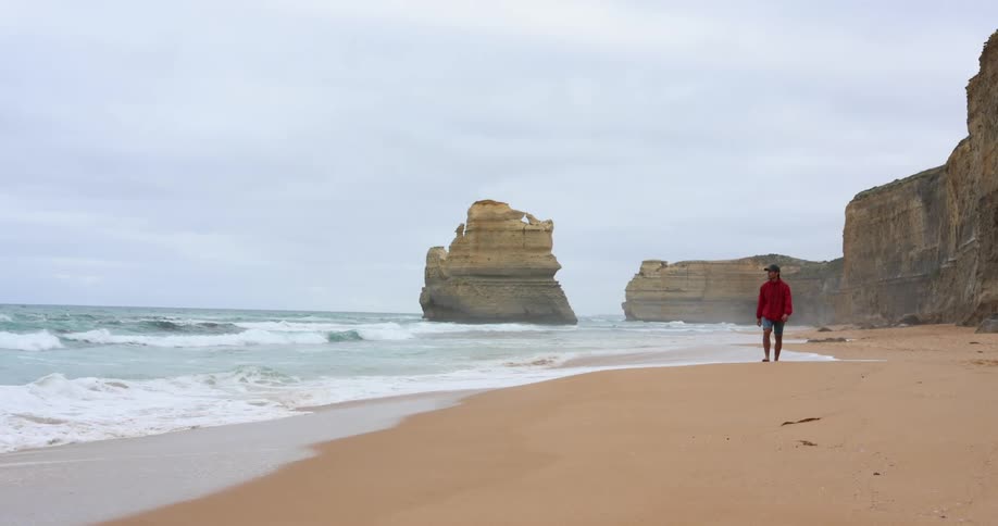 A man walks alone on an empty beach where the ocean meets the sand