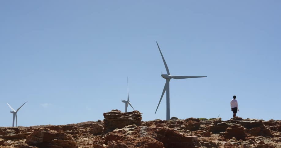 A person standing with wind turbines the sky and clouds in the background