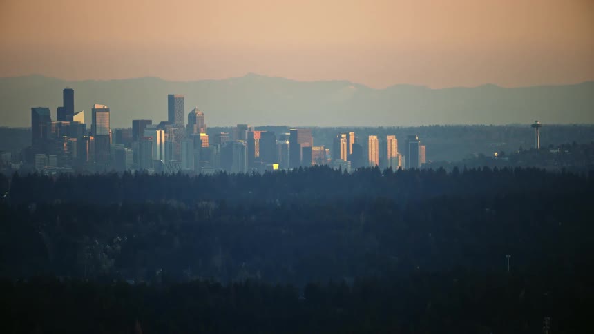 Downtown Seattle skyscrapers and the space needle rise high above the hills of the greater city with the Cascade mountains in the background