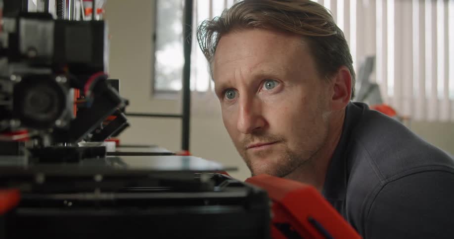 A man crouches down to take a closer look at a 3d printer