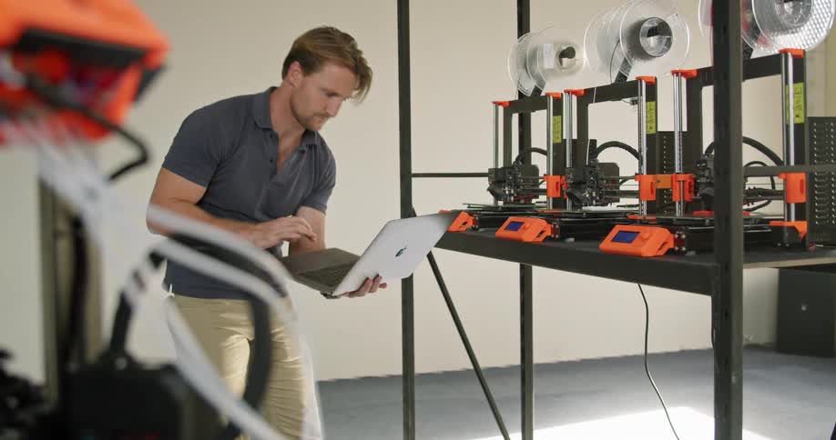 A man holds and uses a laptop to monitor electrical equipment set up on a table