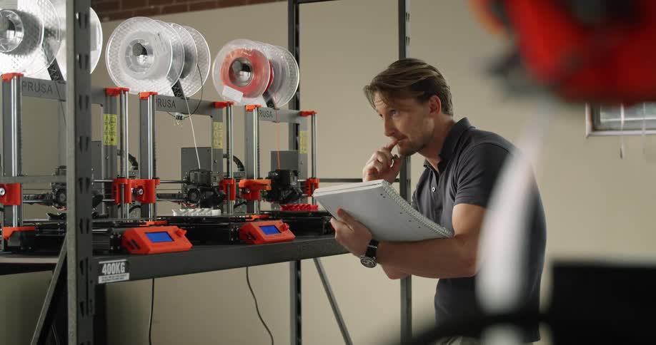 An employee watching 3d printers and taking notes