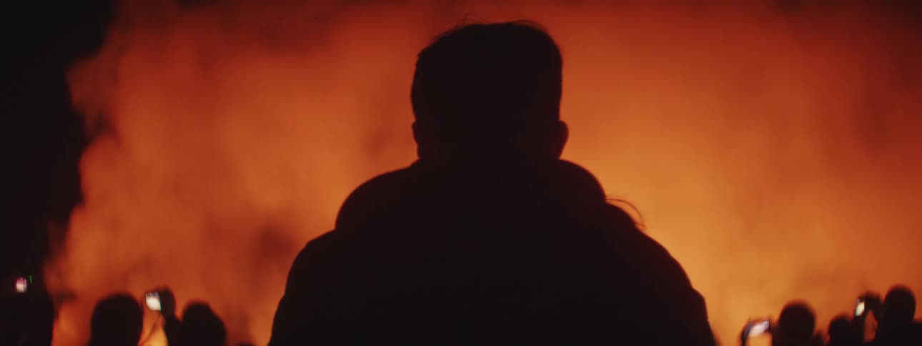 A man pulls a woman back as they head toward a large crowd watching a wildfire burn at night