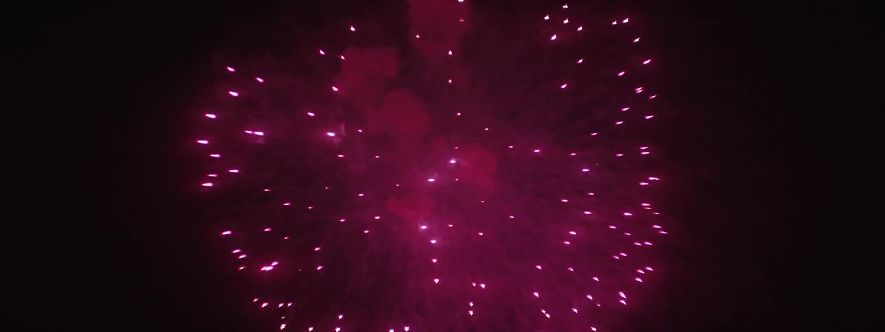 Reddish pink fireworks explode in the night sky