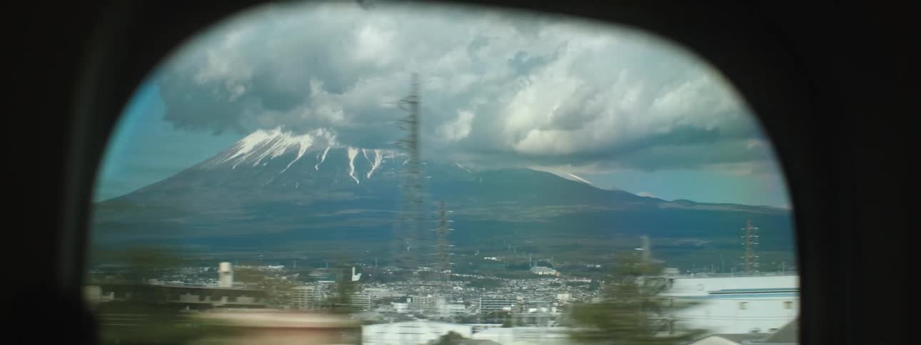 A small window on a train car shows a busy suburb near a mountain range