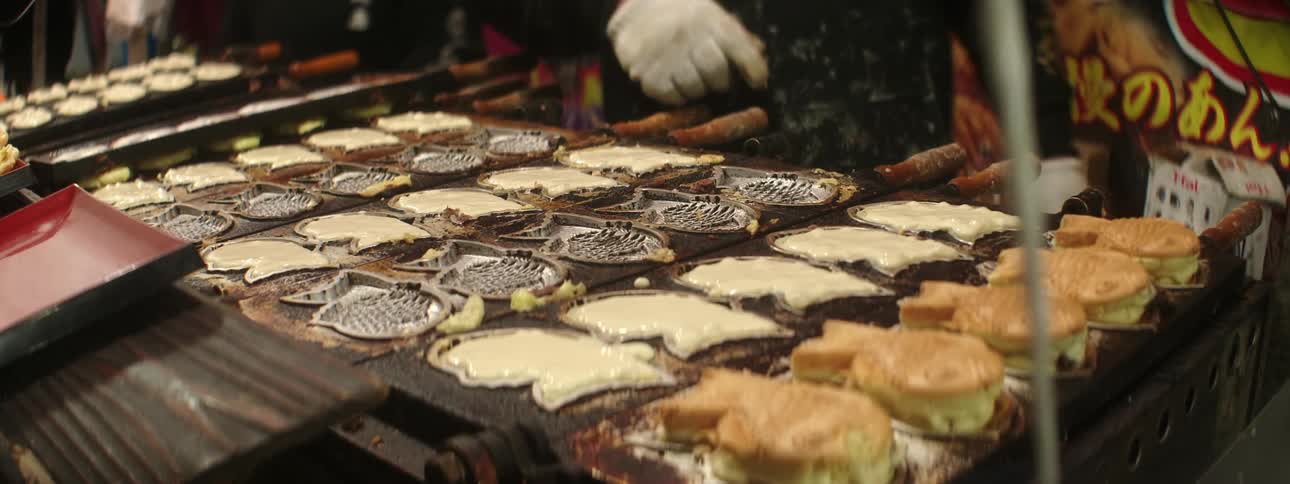 A person cooks various pieces of food on a grill in a marketplace restaurant