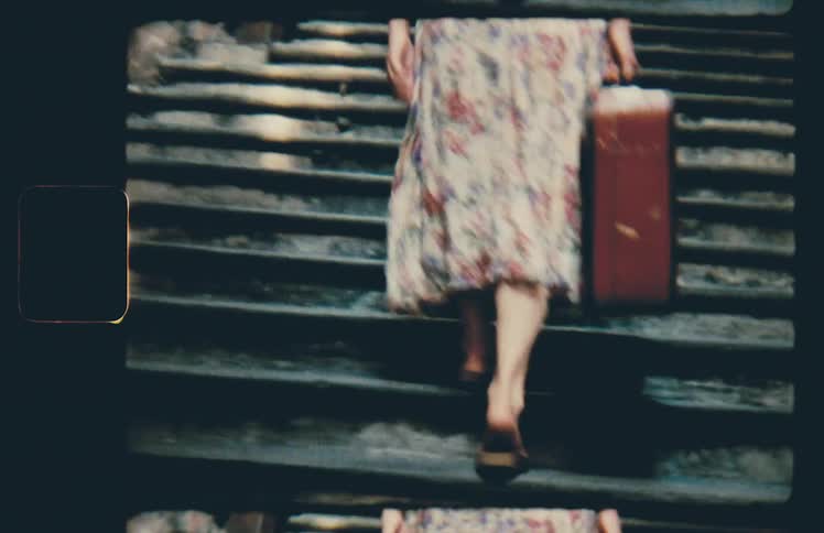 Woman in floral vintage dress carries suitcase up stairs in city neighborhood