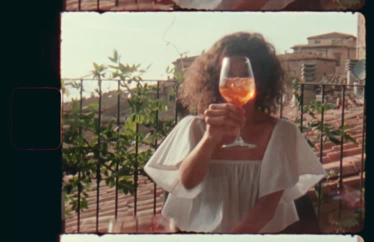 A woman holding a wine glass in front of her face sitting on a balcony on a sunny windy day