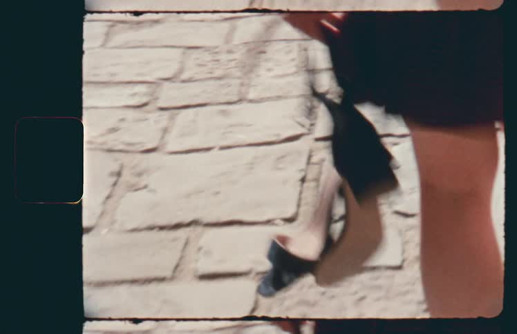 Woman walking down cobblestone path carrying high heels in hand