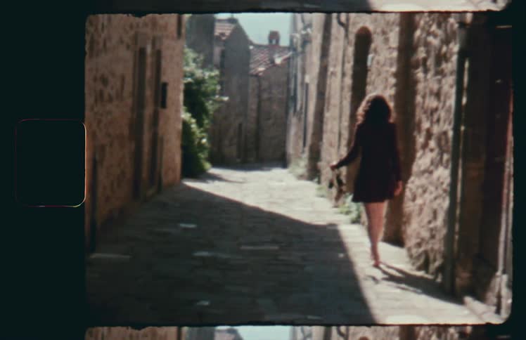 A woman wobbles and spins as she walks barefoot down an alley between buildings