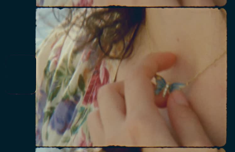 Woman wearing blue butterfly necklace touches pendant with hand