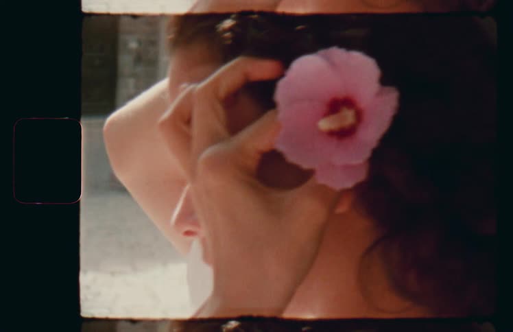 Woman plucks hibiscus flower and places it behind ear in courtyard