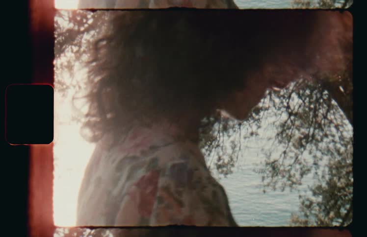 Vintage footage of woman in floral dress walking in front of ocean