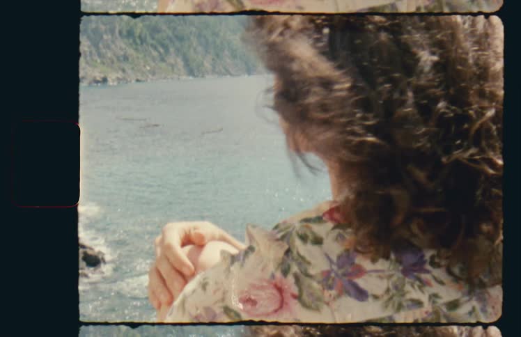 Woman faces wind standing near ocean facing promontory