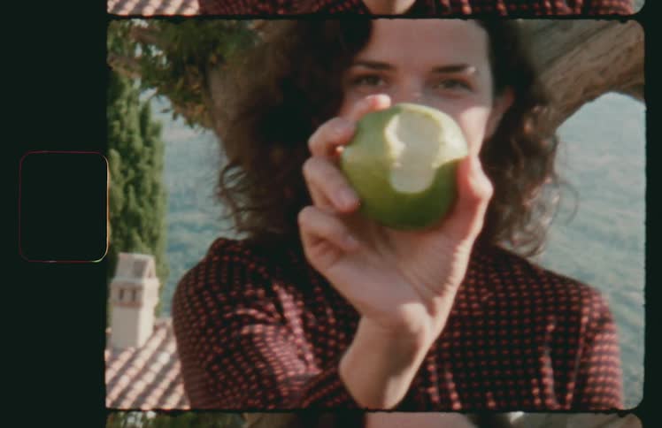 A woman holding an apple with trees in the background
