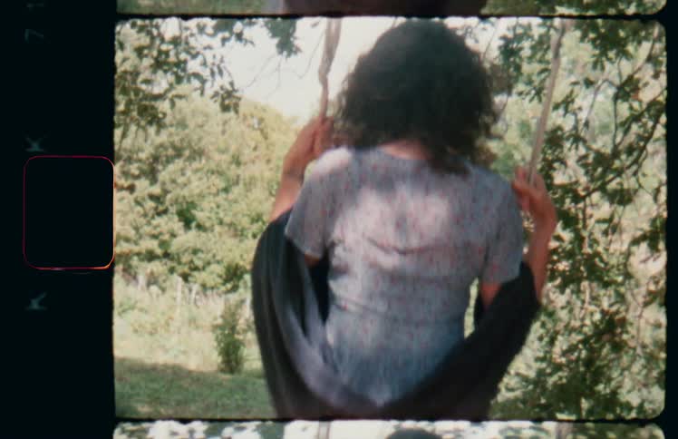 A woman with a shawl draped over her arms swings on a tree swing on a sunny day