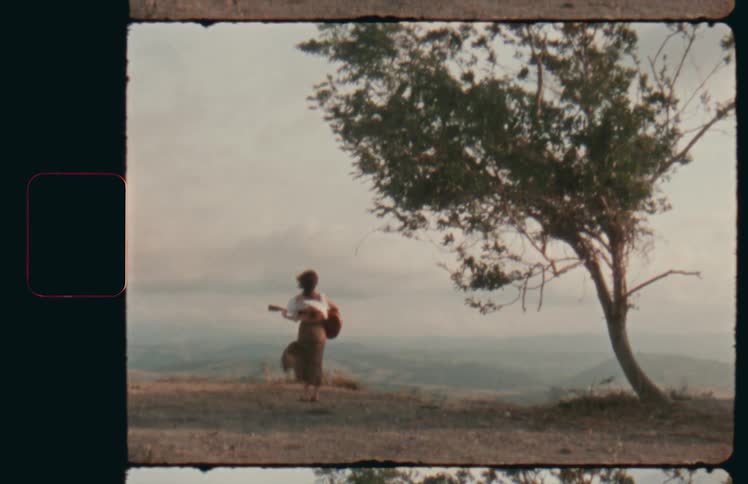 Vintage footage of woman in dress playing guitar on hillside overlooking valley
