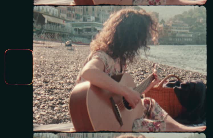 A person sits on the coastal beach playing the guitar