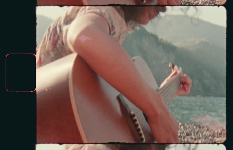 A woman on a shore playing an acoustic guitar