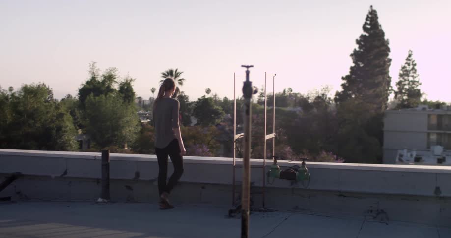 A woman walks to the ledge of the top of a building