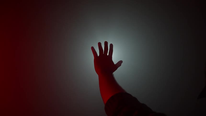 A raised arm and hand try to block the glare of a light