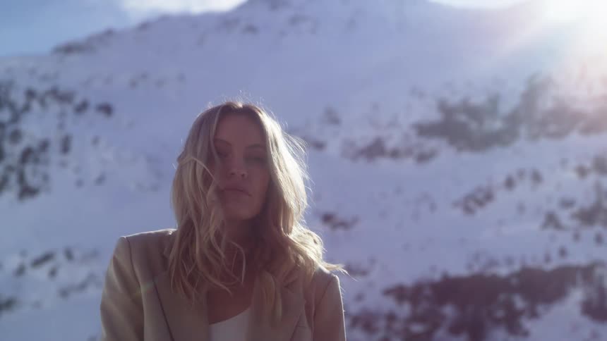 Blonde woman with a beige blazer stands in front of high snowy mountain