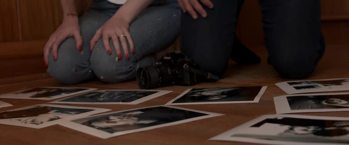 A man and woman kneeling on a floor next to a camera and photographs