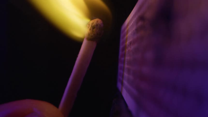 A person lights a match on a matchbox and immediately presses it against the box to put out the flame