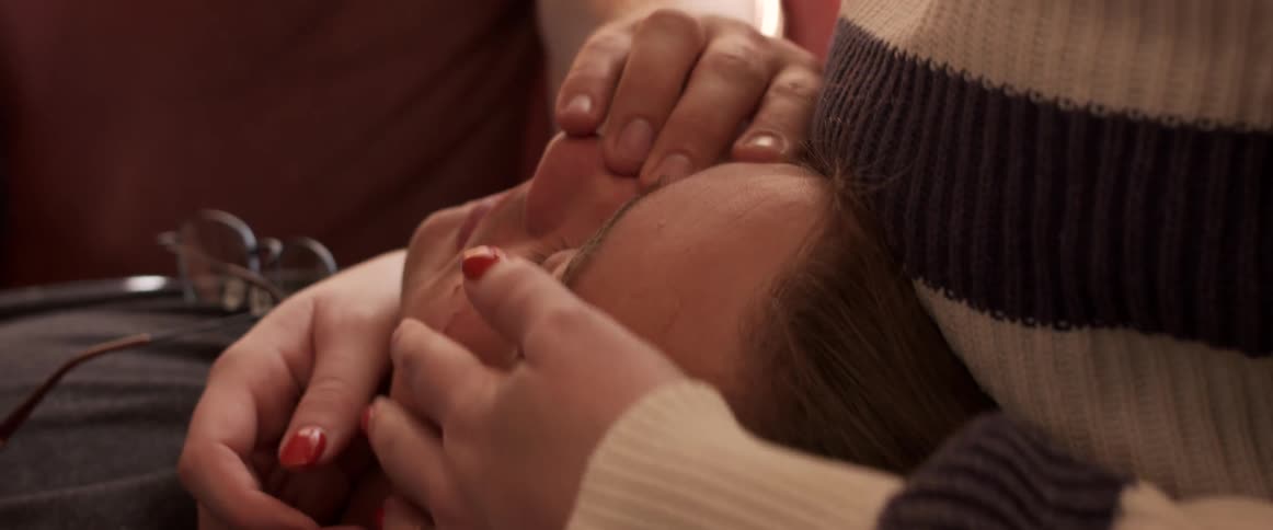 A woman with a sweater caressing a mans face with a glasses on his chest
