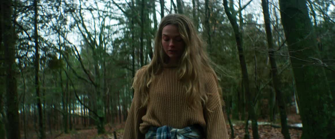 A young woman walks leisurely through a woodland during the day