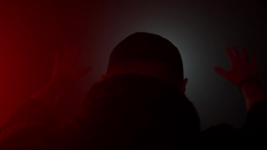 Man walks away with hands raised under red and black lighting