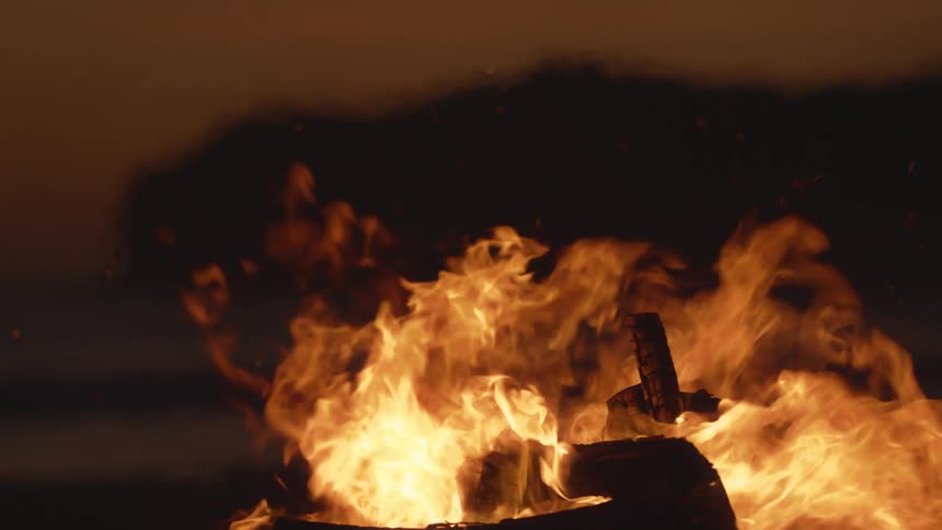 Wood burning with fire embers and smoke with the sky and clouds in the background