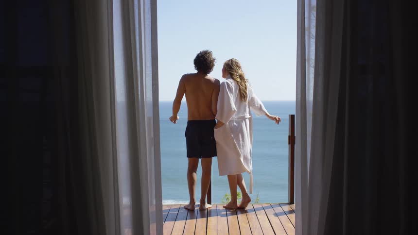A man and woman standing on a balcony overlooking a beach on a sunny day