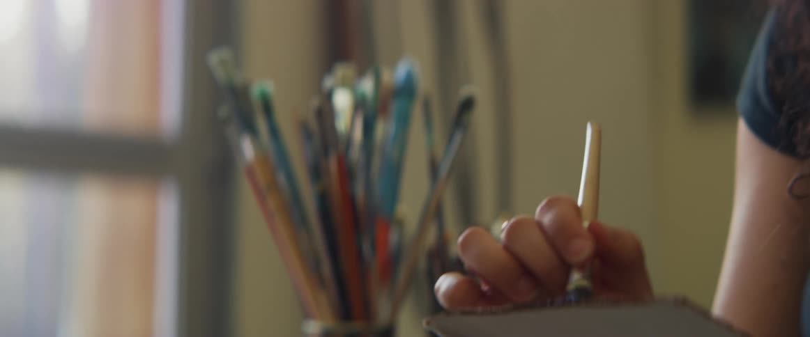 A woman holds a small palette as she paints on a large canvas indoors