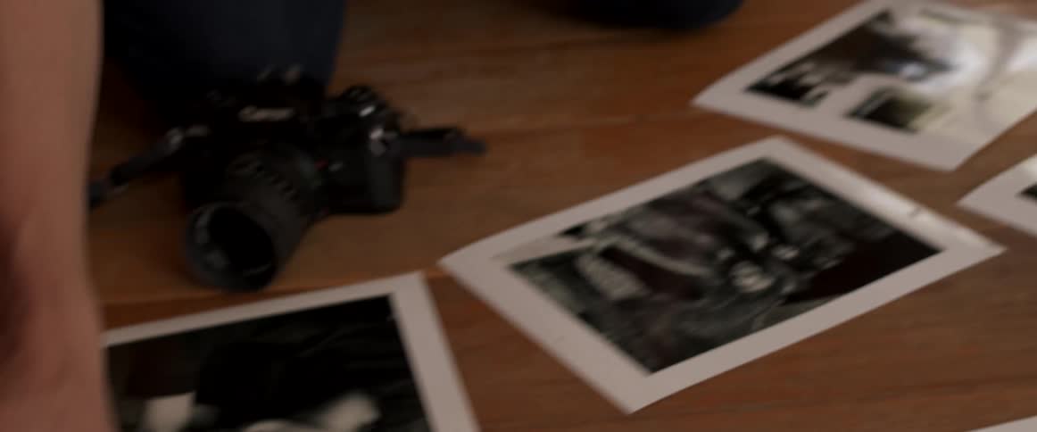 Two women are kneeling on a wood floor with many photos and a camera in front of them