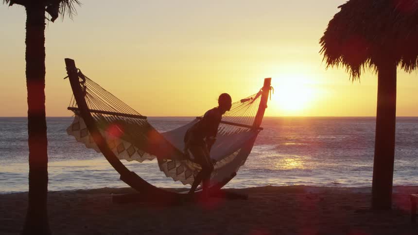 A woman walks over and lays on the hammock