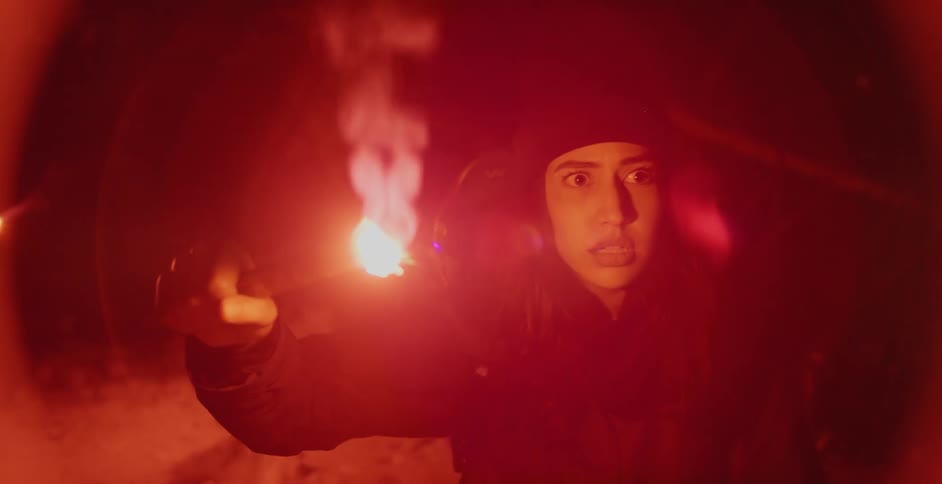 Scared woman waving a red flare in the forest at night