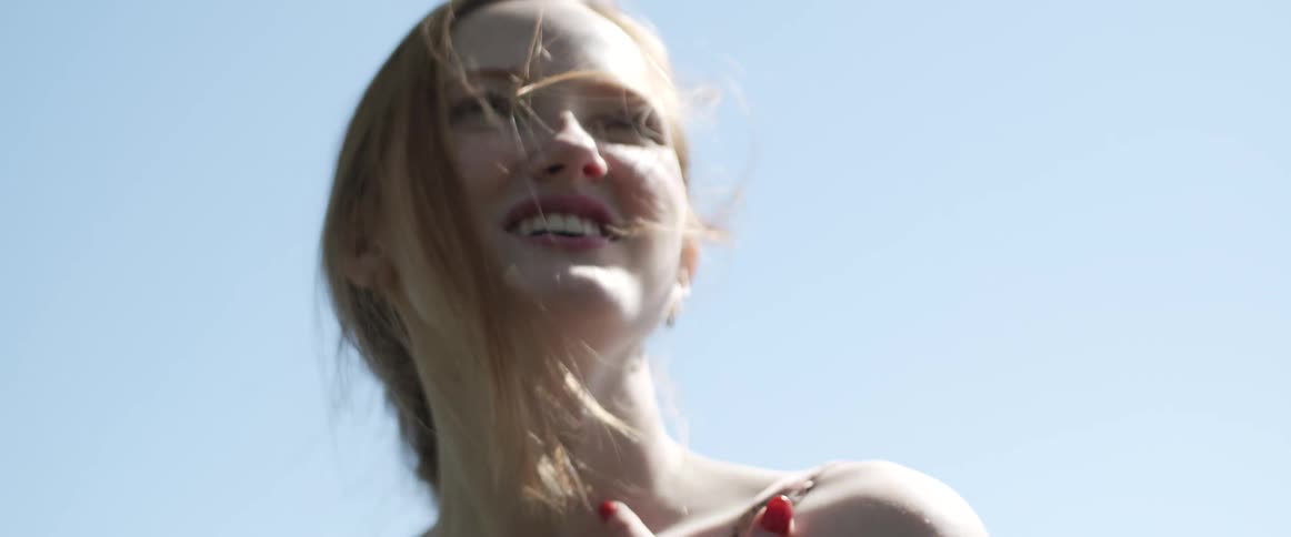 A blonde teenage girl smiling and laughing while standing outside on a sunny day