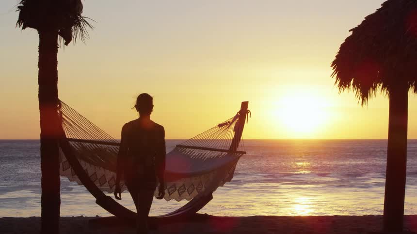 Young woman walking near a hammock in a tropical beach at sunset