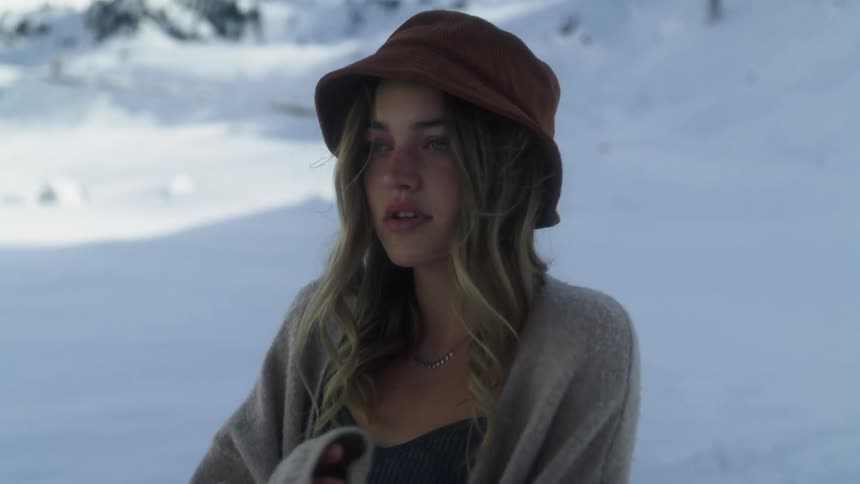 A woman standing outside in snow crosses her arms and closes her sweater during the day