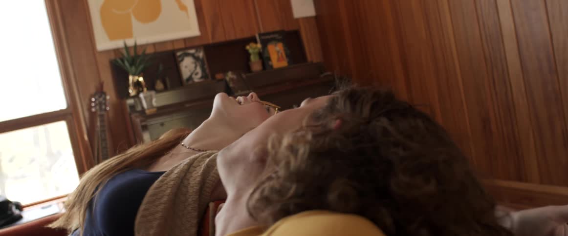 A man and a woman in a room sitting on a couch with a wall and window in the background